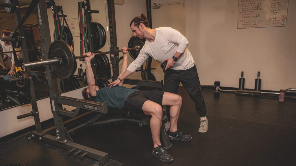 Trainer helping mail client lift a barbell at our Bay Area gyms